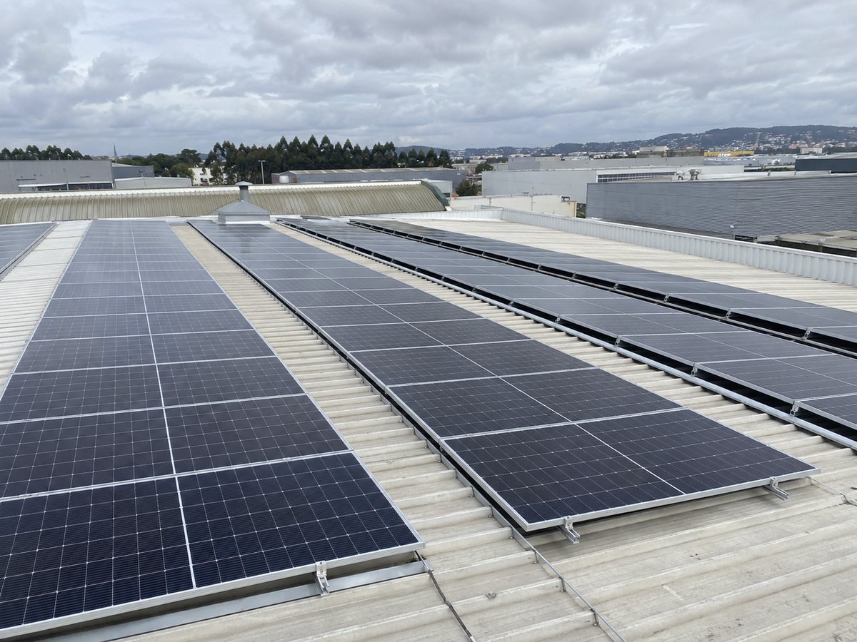 Imagem ilustrativa de filas de painéis solares sobre a cobertura metálica de um pavilhão industrial.