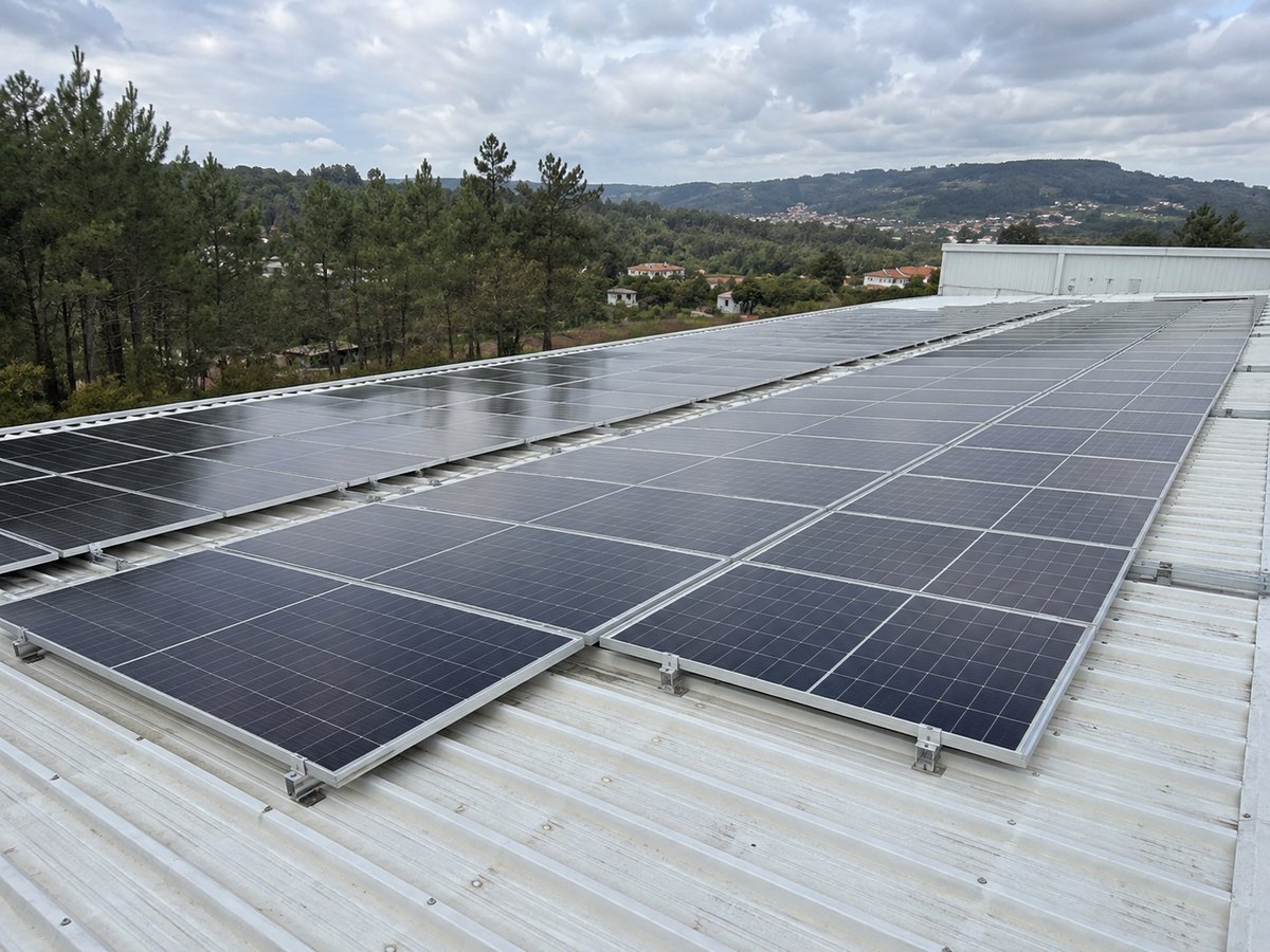 Imagem ilustrativa de uma instalação solar num pavilhão industrial sob um céu parcialmente nublado.
